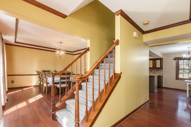 stairway with a chandelier, ornamental molding, baseboards, and wood finished floors