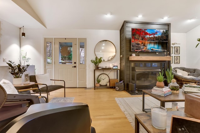 living area featuring light wood-style floors, lofted ceiling, and a large fireplace