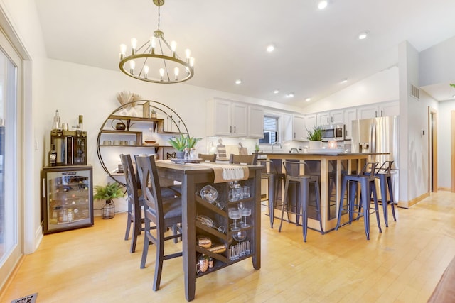 dining room with light wood-style flooring, wine cooler, visible vents, and vaulted ceiling