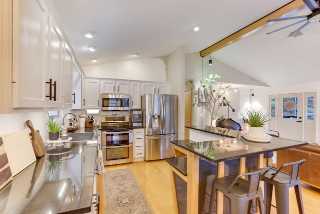 kitchen featuring appliances with stainless steel finishes, light wood-type flooring, vaulted ceiling with beams, and a sink