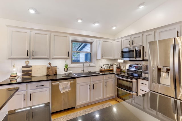 kitchen with stainless steel appliances, lofted ceiling, a sink, and dark countertops