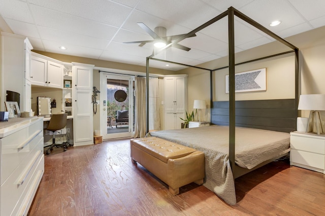 bedroom with access to exterior, a drop ceiling, dark wood finished floors, and built in desk