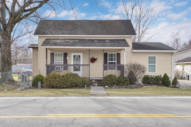 view of front of house featuring a porch, a front yard, fence, and a shingled roof