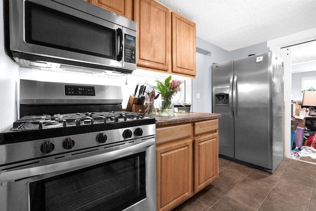 kitchen with appliances with stainless steel finishes, dark tile patterned flooring, and a textured ceiling