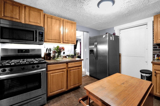 kitchen featuring brown cabinets, stainless steel appliances, a textured ceiling, and dark tile patterned flooring