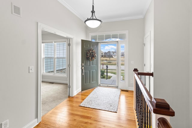 entrance foyer with baseboards, light wood-style flooring, visible vents, and crown molding