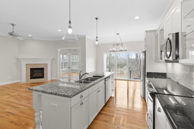 kitchen featuring light wood-style flooring, a sink, a high end fireplace, appliances with stainless steel finishes, and a wealth of natural light