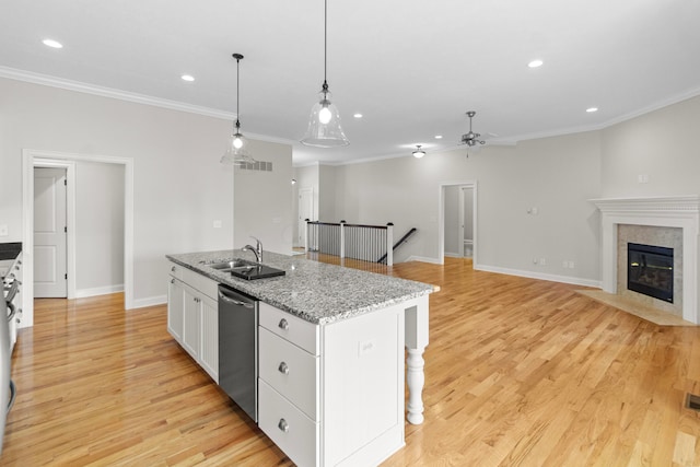 kitchen featuring white cabinets, dishwasher, light wood-style flooring, a kitchen island with sink, and a sink