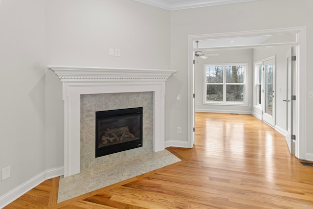 unfurnished living room with baseboards, a premium fireplace, wood finished floors, and crown molding