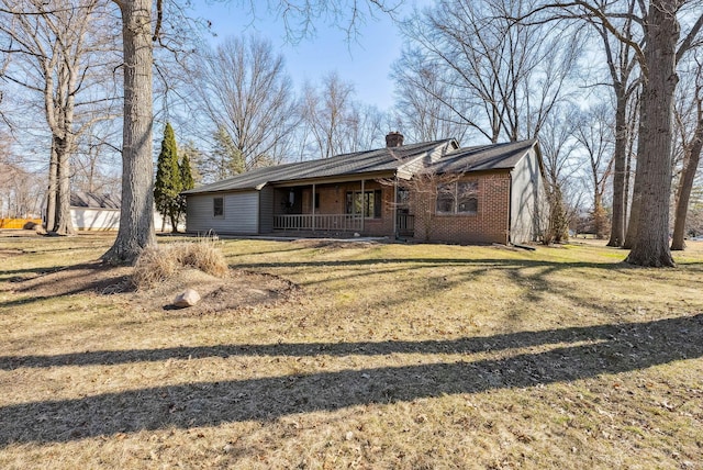 view of front of home featuring a front lawn, brick siding, covered porch, and a chimney