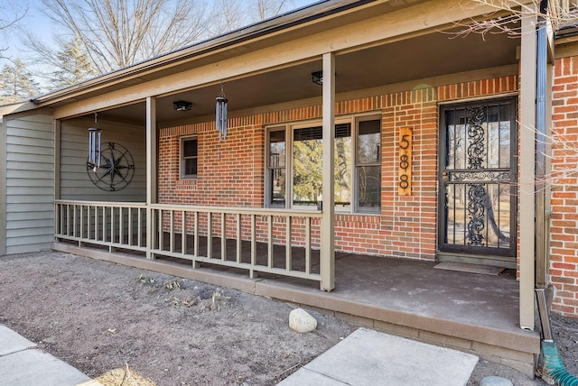 view of exterior entry with a porch and brick siding