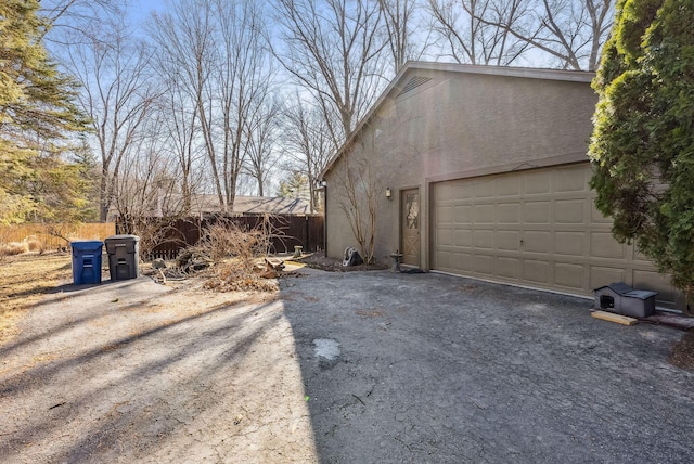 view of property exterior with stucco siding, a garage, driveway, and fence