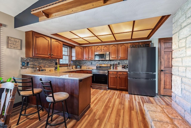 kitchen with light wood finished floors, decorative backsplash, appliances with stainless steel finishes, and a peninsula