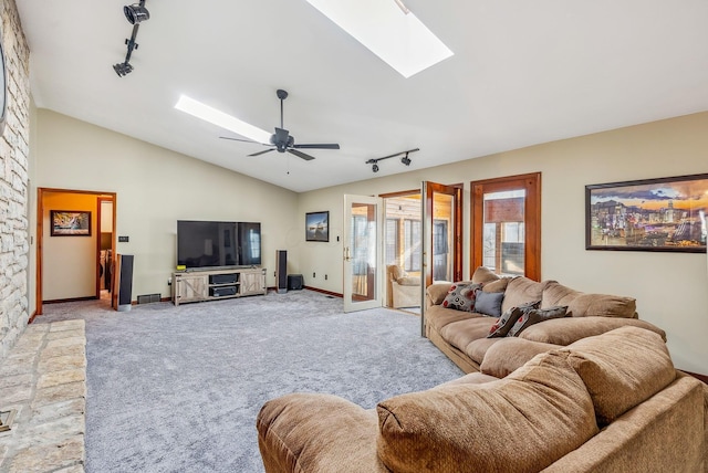 carpeted living room with vaulted ceiling with skylight, rail lighting, baseboards, and ceiling fan