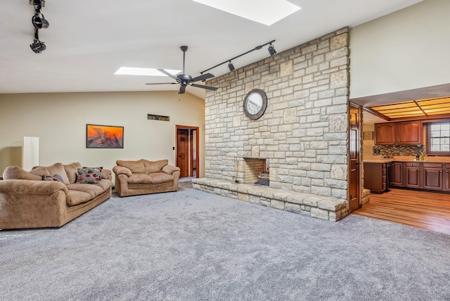 living room featuring track lighting, ceiling fan, light colored carpet, vaulted ceiling with skylight, and a fireplace