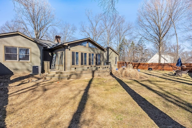 back of property featuring central AC unit, fence, a lawn, and a chimney