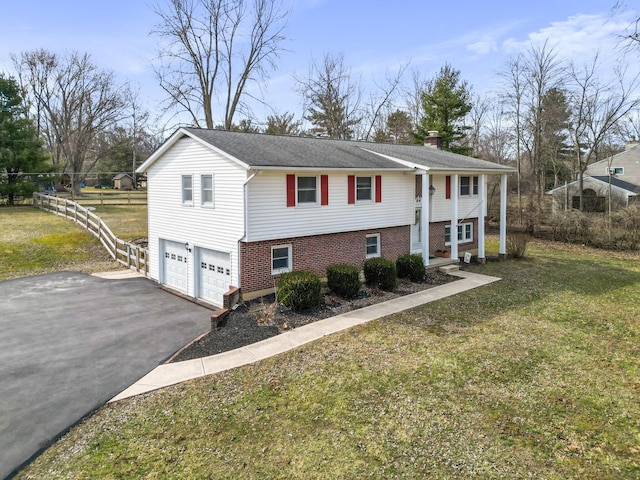 raised ranch with driveway, a garage, brick siding, fence, and a front yard