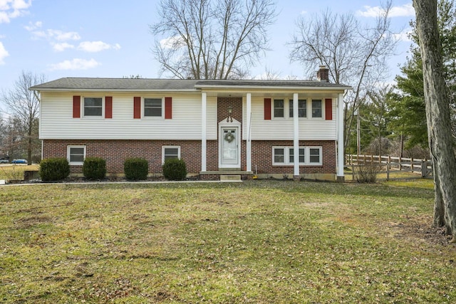 bi-level home featuring brick siding, fence, a chimney, and a front lawn