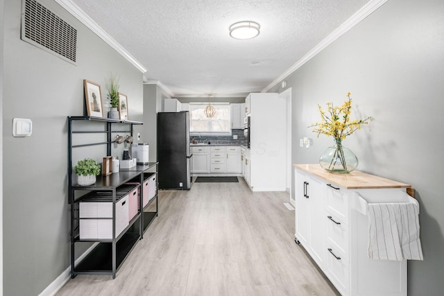 kitchen featuring visible vents, light wood-style floors, freestanding refrigerator, ornamental molding, and white cabinets