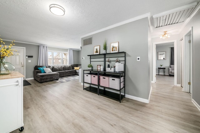 living area featuring a textured ceiling, ornamental molding, light wood-type flooring, and visible vents