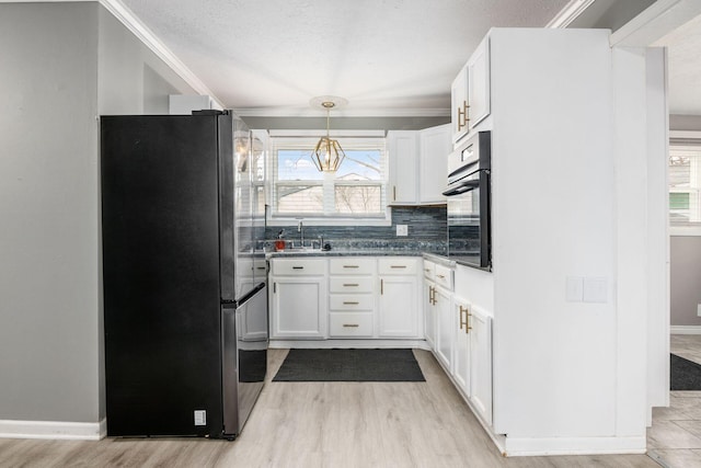 kitchen with white cabinetry, oven, freestanding refrigerator, and a healthy amount of sunlight