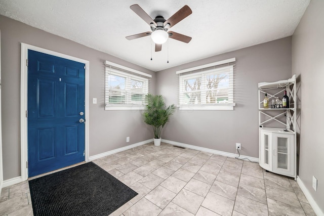 foyer with ceiling fan, a textured ceiling, and baseboards