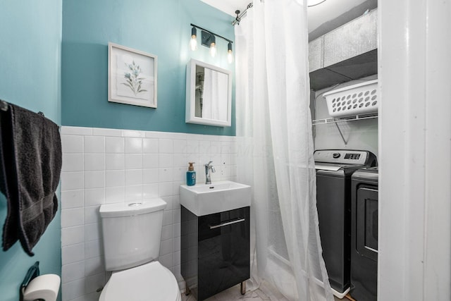 bathroom featuring toilet, a wainscoted wall, a sink, tile walls, and washer and dryer