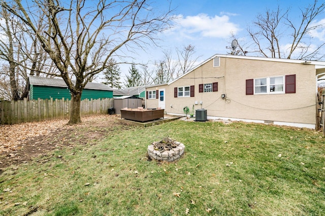 back of property with central AC unit, a jacuzzi, a fire pit, fence, and a yard