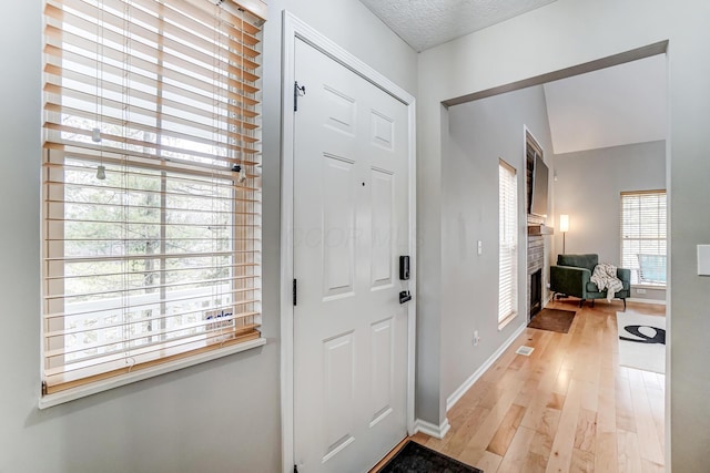 entryway featuring a textured ceiling, light wood-type flooring, a fireplace, and baseboards