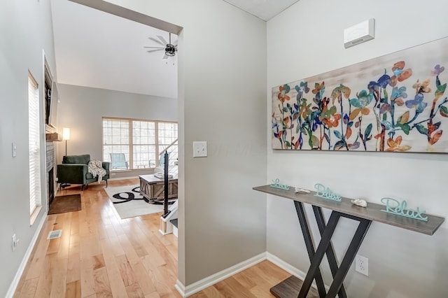 hallway with a high ceiling, visible vents, light wood-style flooring, and baseboards