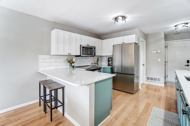 kitchen with light wood-style flooring, a peninsula, visible vents, appliances with stainless steel finishes, and decorative backsplash