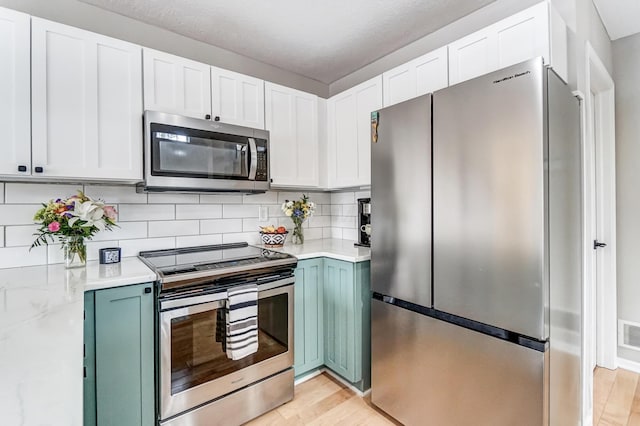 kitchen featuring white cabinets, light wood-style flooring, stainless steel appliances, and decorative backsplash