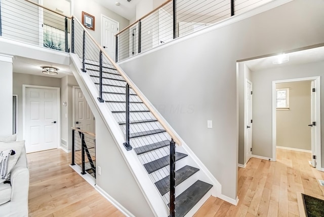 stairs featuring a high ceiling, baseboards, and wood finished floors