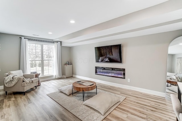 living room with arched walkways, baseboards, a glass covered fireplace, and light wood finished floors