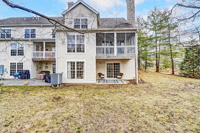 back of property with a sunroom, a patio area, a lawn, and a chimney