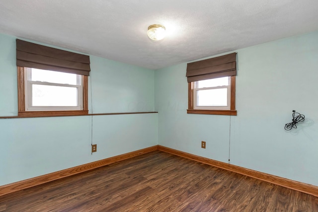 empty room with dark wood-type flooring, a textured ceiling, and baseboards