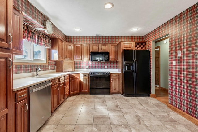 kitchen featuring light countertops, brown cabinetry, a sink, black appliances, and wallpapered walls