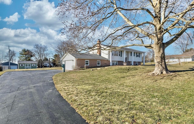 view of front facade with driveway, brick siding, a chimney, and a front yard