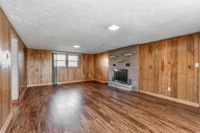 unfurnished living room with a brick fireplace, wooden walls, a textured ceiling, and wood finished floors