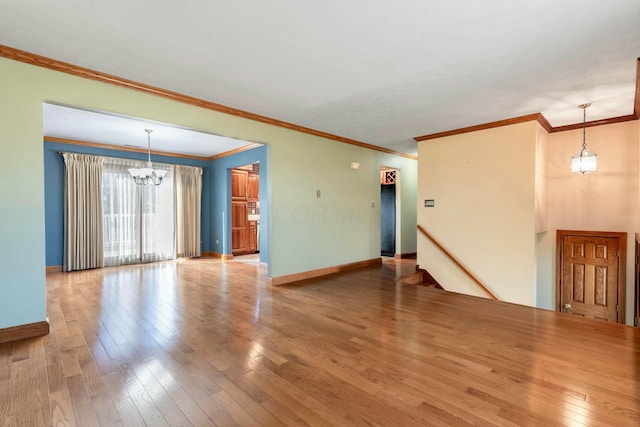 unfurnished living room with wood-type flooring, baseboards, a chandelier, and crown molding