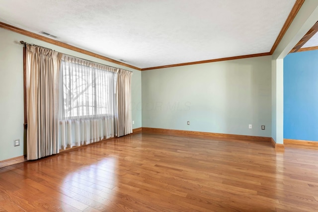 spare room featuring ornamental molding, wood finished floors, visible vents, and baseboards