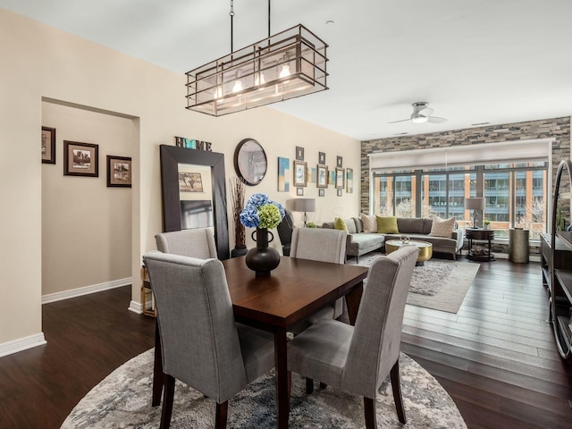 dining space featuring dark wood-style flooring, baseboards, and ceiling fan with notable chandelier