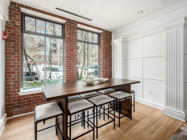 dining space featuring light wood-style floors, brick wall, and a wealth of natural light