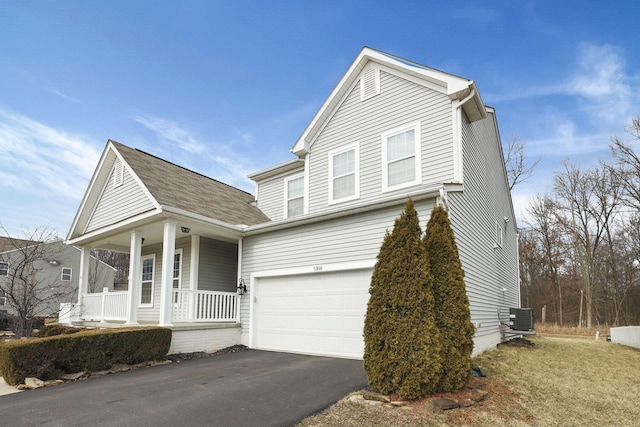 traditional-style house featuring covered porch, driveway, central AC unit, and a garage