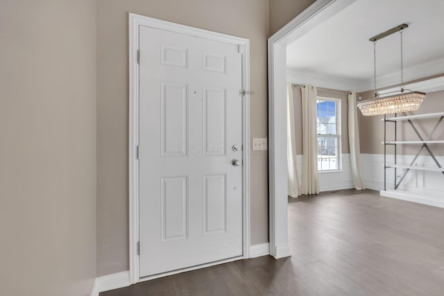 entrance foyer featuring a wainscoted wall, crown molding, dark wood-style flooring, and a notable chandelier