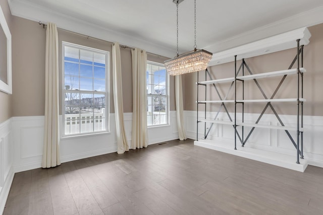 unfurnished dining area with dark wood-type flooring, a wainscoted wall, a notable chandelier, and ornamental molding