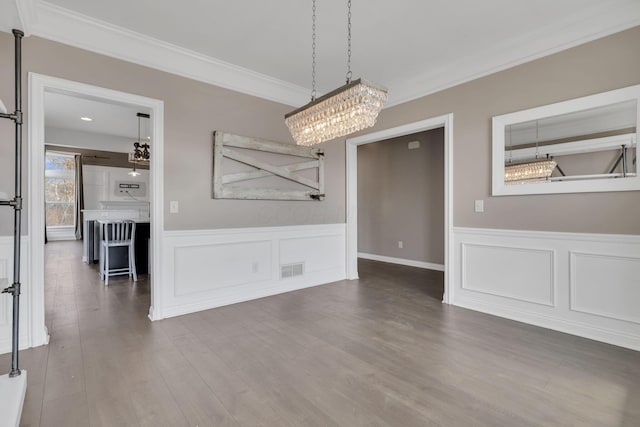 unfurnished dining area with visible vents, wainscoting, wood finished floors, an inviting chandelier, and crown molding