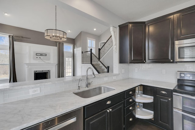 kitchen with decorative backsplash, an inviting chandelier, appliances with stainless steel finishes, a sink, and light stone countertops