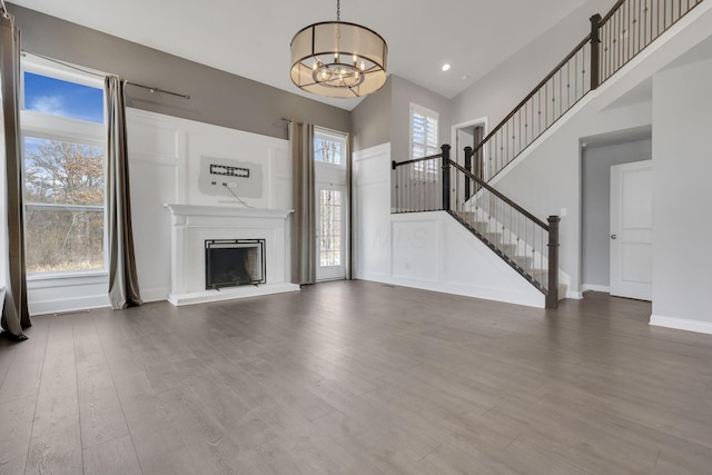 unfurnished living room featuring baseboards, a fireplace with raised hearth, dark wood-type flooring, an inviting chandelier, and stairs