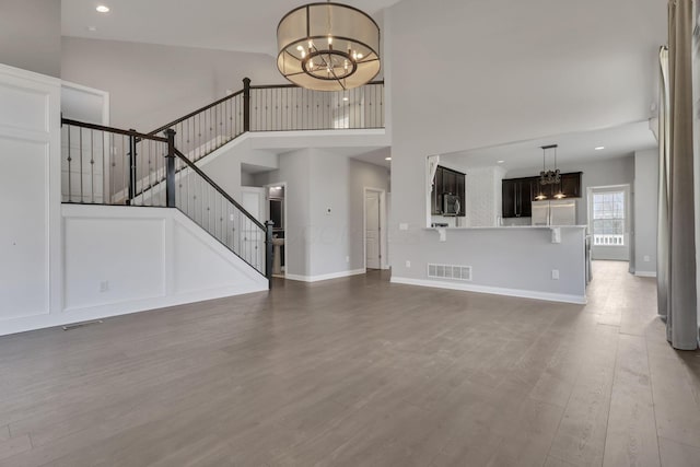 unfurnished living room with a chandelier, stairs, wood finished floors, and visible vents